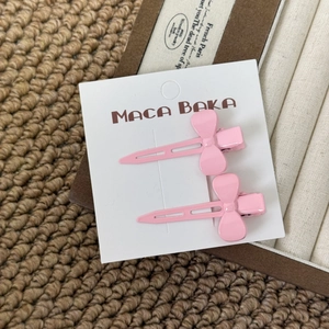 Detail of two pink metal bow hair clips on a white card against a textured background