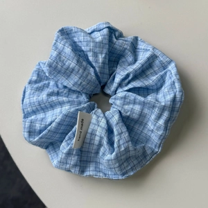 Detailansicht eines hellblau-karierten Scrunchies aus Stoff mit Handmade-Etikett
