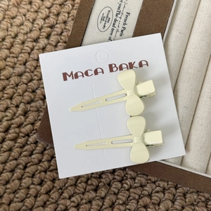 Close-up of two creamy yellow bow-shaped hair clips on a white card display