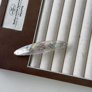 Macro detail of oval acetate hair clip with shimmering rhinestones and pearly finish