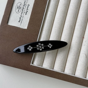 Detailed close-up of a vintage black oval hair clip with sparkling rhinestone flower motifs