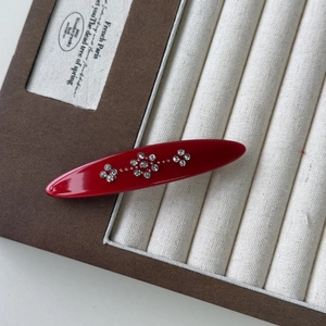 Detail of red acrylic hair clip with sparkling rhinestone flower pattern in jewelry box
