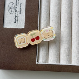Détail des motifs ours et cerise sur une pince à cheveux en acrylique dans un écrin