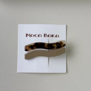Detail of wave-shaped acetate hair clips in tortoiseshell and solid brown on card
