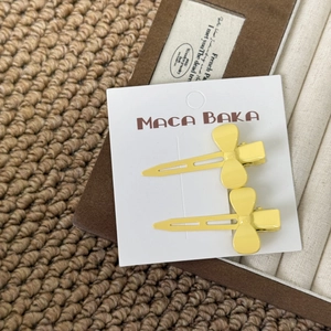 Detail of two yellow bow hair clips on a white card over a warm textured background