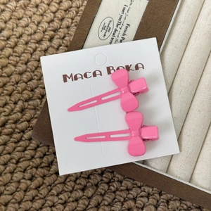 Close-up of pink bow hair clips in a smooth matte finish on a branded display card