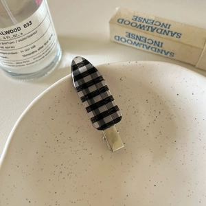 Detail view of a black and white checkered hair clip on a minimalist ceramic plate