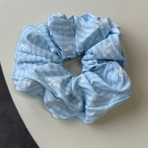 Gros plan d'un chouchou bleu clair avec motif nœud blanc et tissu à texture rayée