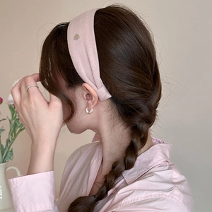 Detailed side view of a pink wide fabric headband with a silver heart-shaped metal logo