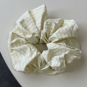 Détail d'un chouchou en tissu à rayures jaunes et blanches avec motif petits nœuds