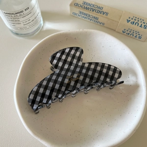 Detail view of a black and white checkered hair claw clip with golden text in a ceramic dish