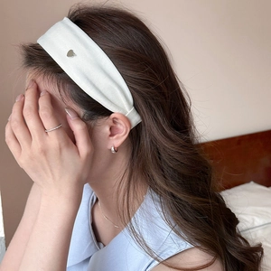Detail of white ribbed headband with silver heart charm on model in soft profile view