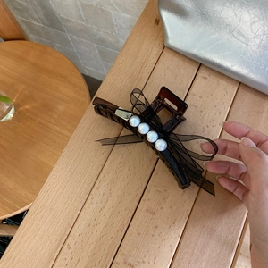 Makro-Detail der bernsteinfarbenen Haarklammer mit schwarzer Netzschleife und Perlen