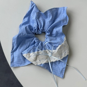 Detailed view of blue plaid hair scrunchie with white lace edges and a light blue bow