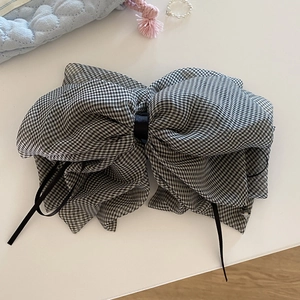 Detail view of a large black and white checkered bow hair clip with black silk ribbons