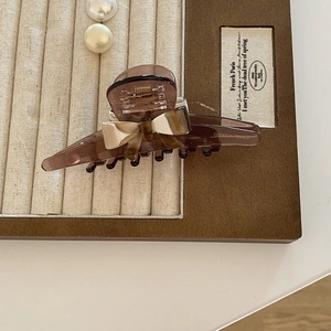 Elegant tortoiseshell acetate bow hair claw clip with gold French text on a beige tray