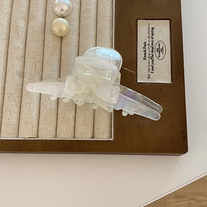 Detail view of the iridescent acetate bow hair claw clip on a luxury velvet display tray