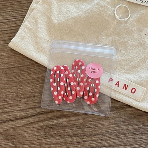 Detailed view of four red polka dot BB hair clips in a small transparent zipper pouch