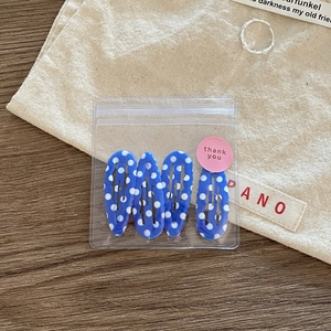 Detail showing set of four blue and white polka dot teardrop hair clips in a clear pouch