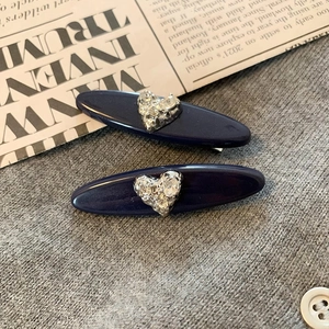 French style dark blue hair clips with crystal heart accents on grey fabric background