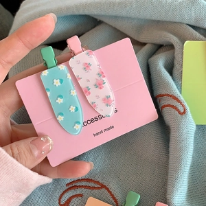 Gros plan d'un lot de barrettes à fleurs vert menthe et rose sur carte cadeau
