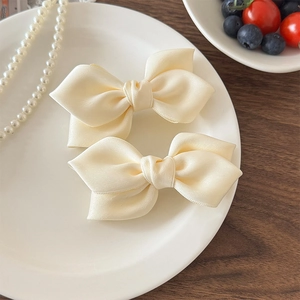 Paire de barrettes à nœuds en satin crème pour femmes sur une assiette décorative