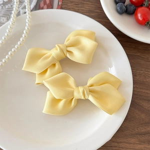 Détail de deux barrettes à nœuds en satin jaune vif posées sur une assiette blanche