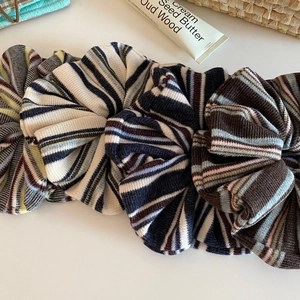 Three retro striped knitted scrunchies in cream, blue, and brown on a white surface