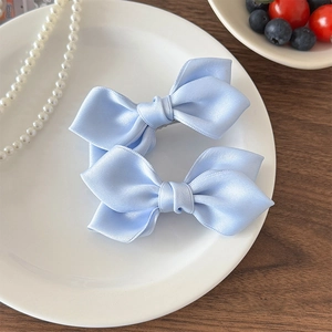 Détail de deux barrettes à nœuds en satin bleu clair sur une assiette blanche