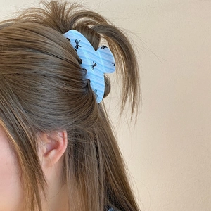 Detail view of light blue striped acrylic claw clip with black ribbon bow patterns