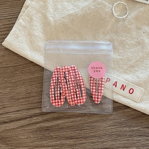 Detailed view of red and white checkered BB hair clips in a transparent thank you package