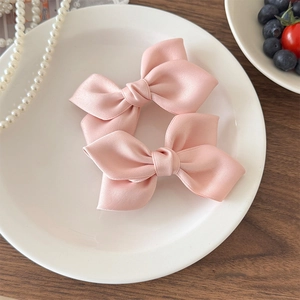 Détail de barrettes nœuds en satin rose sur plateau en céramique avec perles et fruits