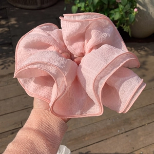 Close-up of pink oversized fabric scrunchie showing delicate micro-grid texture and soft pleats