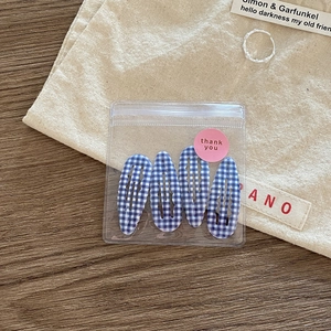Close-up of four blue and white checkered hair clips in transparent packaging on wood