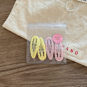 Detail view of four checkered wave-edge hair clips in pink and yellow with thank you gift bag