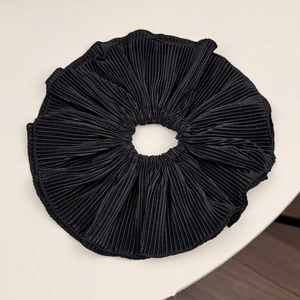 Vue détaillée d'un chouchou en tissu plissé noir avec des bords cousus fins