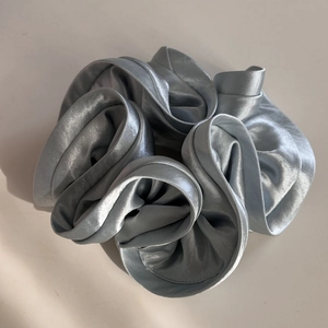 Macro shot of oversized silver-grey satin scrunchie with pleated texture and silky metallic luster