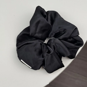 Détail d'un chouchou en satin noir brillant avec des plis souples sur fond neutre