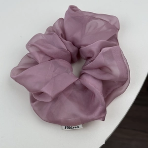 Detailaufnahme von rauchviolettem Organza-Scrunchie mit weichen Falten und Etikett