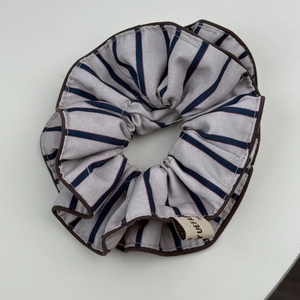 Détail d'un chouchou en tissu à rayures bleues avec bord marron et étiquette de marque