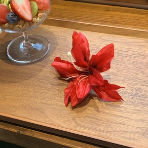 Red lily artificial hair clip for vacation style on a rustic wooden tray with fruit