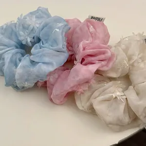 Three-piece set of mesh scrunchies with 3D floral appliqués in pastel blue, pink, and white