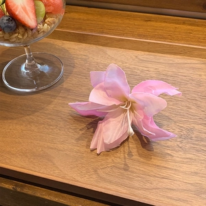 Pink gradient lily hair clip made of silk fabric on a wooden tray with a lifestyle setting