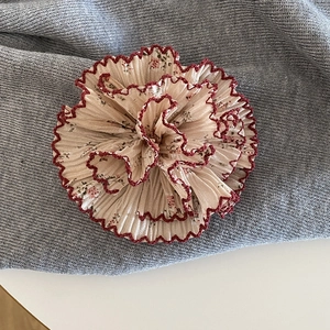 Dettaglio della molletta per capelli a fiori in chiffon con bordi rossi e tessuto plissettato