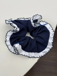 Close-up of navy blue scrunchie with white ruffled edges and small decorative silk bows