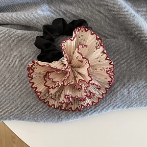 Dettaglio di scrunchie floreale bianco con bordi smerlati rossi su tessuto grigio