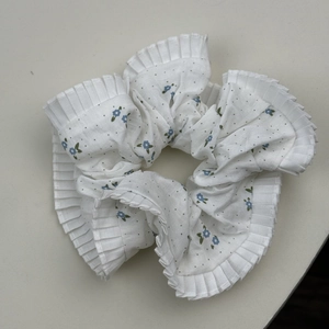 Vue détaillée du chouchou blanc à fleurs bleues avec un design de bord plissé