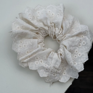 Nahaufnahme von cremefarbenem Spitzen-Scrunchie mit Blumenstickerei und Wellenkante