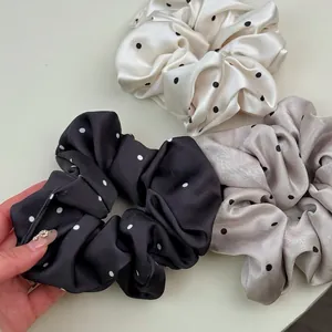 Trois chouchous élégants en satin à pois noir, crème et taupe présentés sur fond neutre