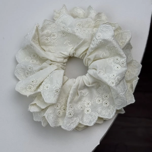 Makroaufnahme von weißem Spitzen-Haargummi mit Blumenstickerei und gewelltem Saum-Design